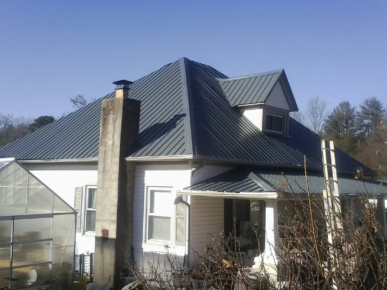 Dark blue standing seam metal roof on a white farmhouse with dormer — Slate & Tile Roof Repair by Roofing Brothers in Aylett