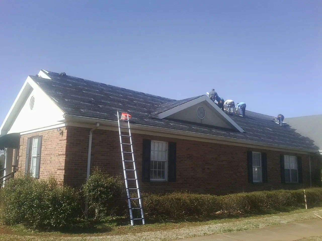 Crew tearing shingles off a brick ranch roof with a ladder set — Emergency Roof Repair work by our crew in Aylett