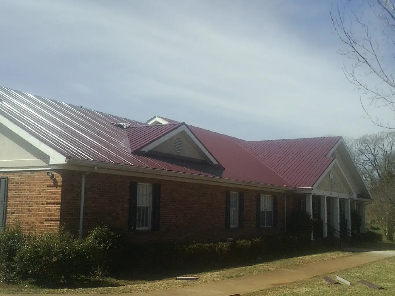Red metal roof with gabled entries on a long brick building, from a Hail Damage Roof Repair job in Aylett