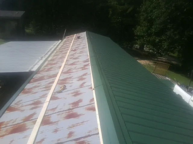 Old rusted panels beside newly installed green metal roofing — Wind Damage Roof Repair by Roofing Brothers in Aylett