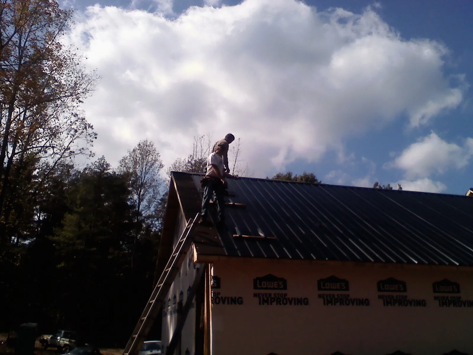 Roofer fastening dark metal panels high against a cloudy sky, from a Roof Inspection job in Aylett