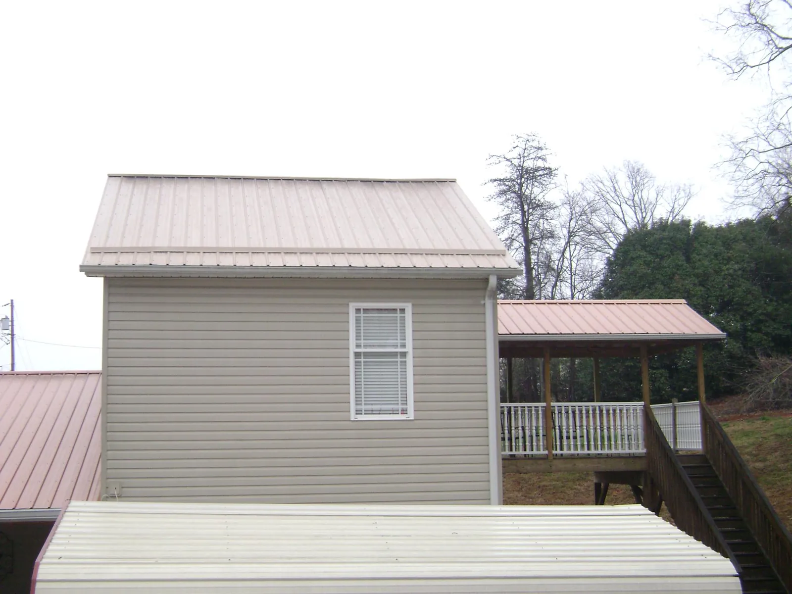 Tan metal roofs on a two story addition and attached porch, from a Roof Replacement job in Aylett